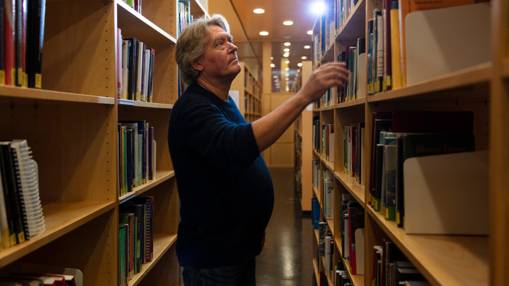 Mann som leter etter en bok på et bibliotek.