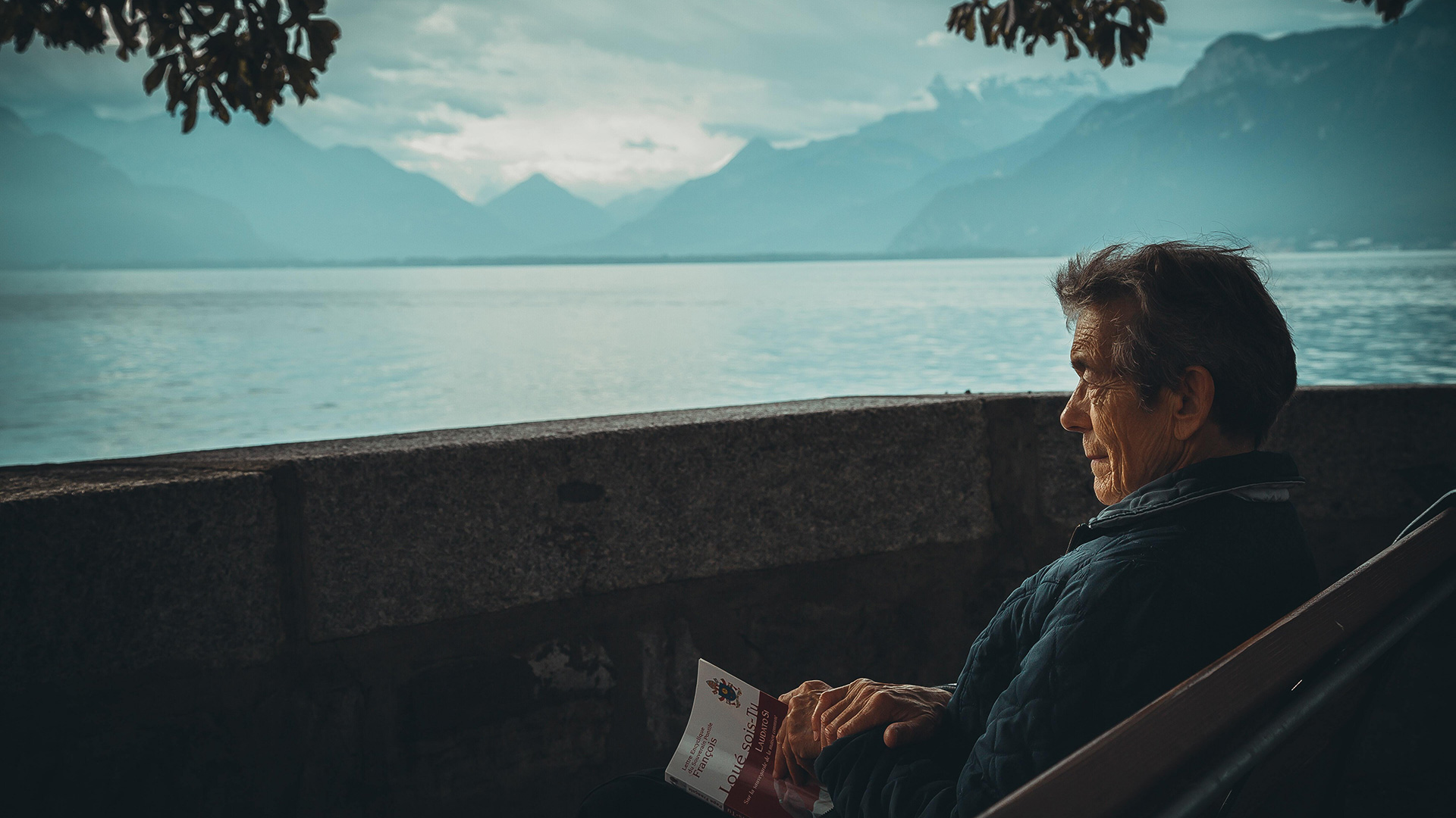 Mann som leser en bok med utsikt over vannet og fjellene.