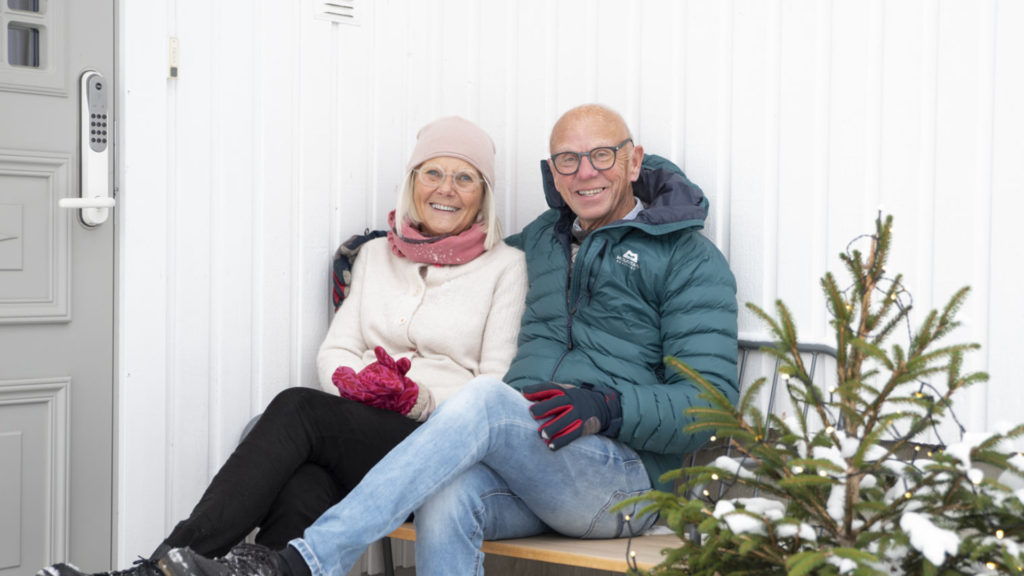 Bilde av et eldre par som sitter utenfor sitt eget hus og smiler.